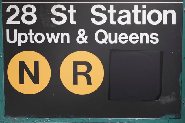 28th Street station after the W train was discontinued in mid-2010. Note the dark grey tape masked over the W bullet. (This sign has since been replaced due to the restoration of the W in 2016.)