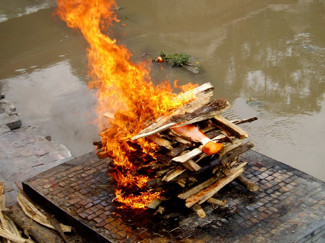 A Hindu cremation rite in Nepal. The samskara above shows the body wrapped in saffron red on a pyre.