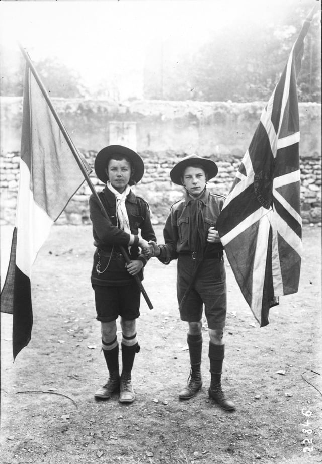 French and British scouts, with their respective national flags, shaking hands. 1912