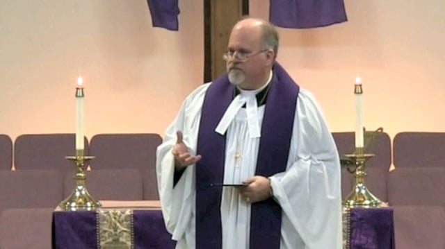 A Methodist minister wearing a cassock, vested with a surplice and stole, with preaching bands attached to his clerical collar