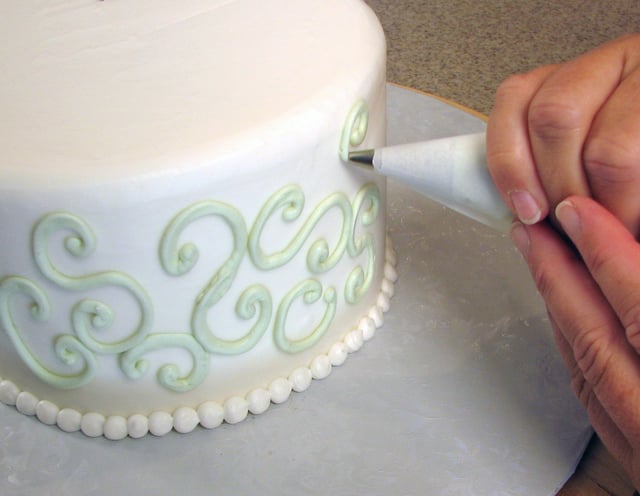 Cake decoration – buttercream swirls being piped onto the sides of this cake with a pastry bag