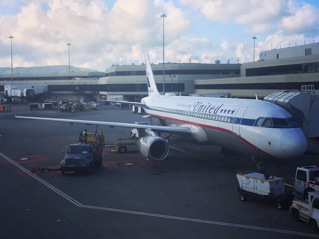 A United Airlines Airbus A320 painted in retro "United Friend Ship" livery sits at a gate at San Francisco International Airport.
