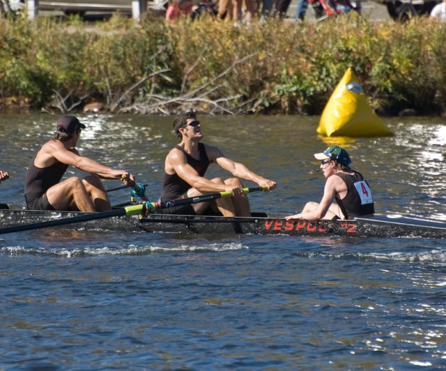 A coxswain (far right) sitting in the stern of the boat, facing the rowers, at the Head of the Charles Regatta.