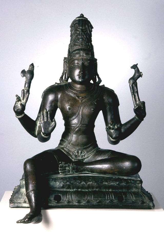 A seated Shiva holds an axe and deer in his hands.