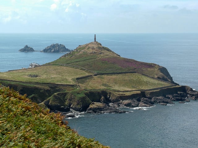 The Heinz Monument (the 1864 chimney of the former Cape Cornwall Mine, visible in the centre) commemorates the purchase of Cape Cornwall for the nation by H. J. Heinz Company. The ruins of St. Helens Oratory can be seen on the left, with the two offshore rocks called.The Brisons in the distance.