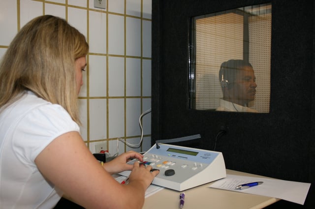An audiologist conducting an audiometric hearing test in a sound-proof testing booth