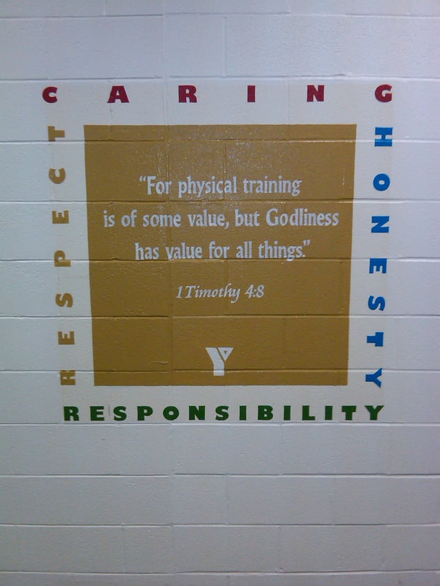 The core values are painted onto a wall of a fitness center in a YMCA, along with a Bible verse, as well as the logo of the YMCA.