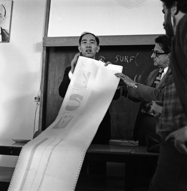 Photo of Kawano in a classroom showing students a script of computations done to produce the art works.