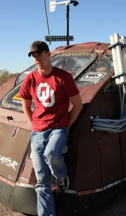 Photo of Joel Taylor standing next the armored tornado vehicle, The Dominator.