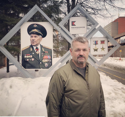 Photo ofLarry Vickers with a portrait of Mikhail Kalashnikov in the background.