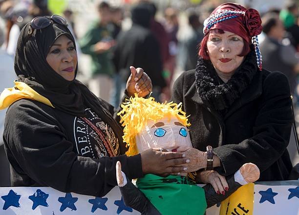 Judy Myers and Rabia Keeble cover the mouth of a Trump pinata during a protest at the California Republican Party Convention.